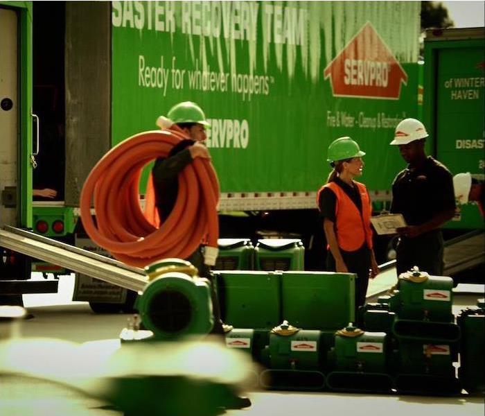  group of 3 SERVPRO reps standing near a green semi truck at a work site