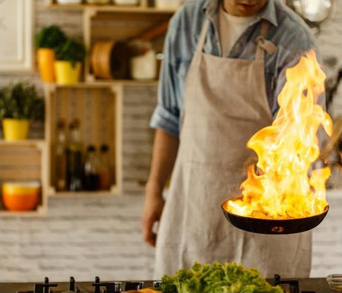 Food on fire burning in a commercial kitchen pan while the chef is cooking