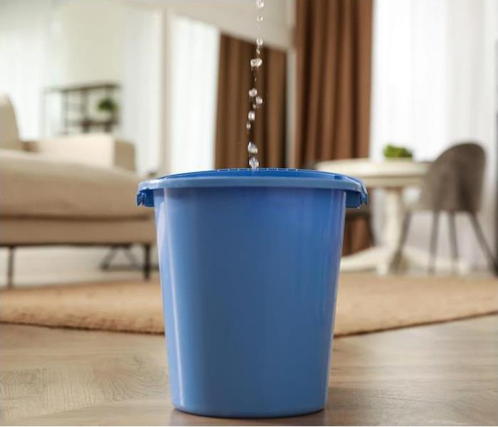 blue bucket in the middle of the living area catching water falling from the ceiling
